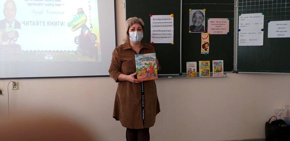 Девушка стоит перед классом у доски и держит в руке книгу