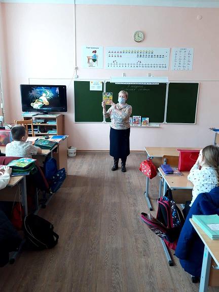 Перед классом стоит девушка и показывает детям книгу