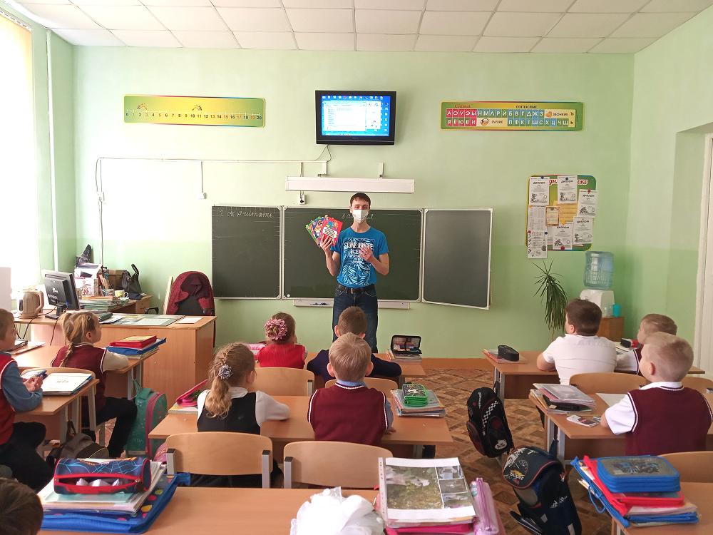 Молодой человек стоит в классе у доски и держит в  руках книги 