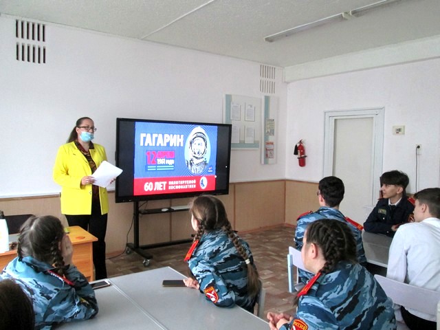 Девуш5ка стоит перед класом на фоне  работающего экрана сизображением космонавта