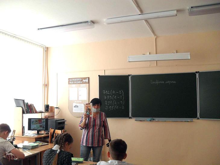 Девушка стоит перед классом и держит в руке книгу.