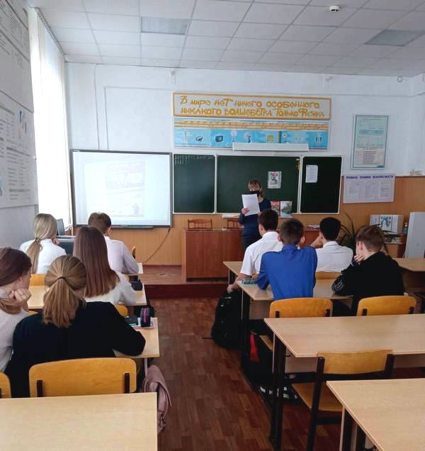 Библиотекарь стоит перд классом и проводит мероприятие.