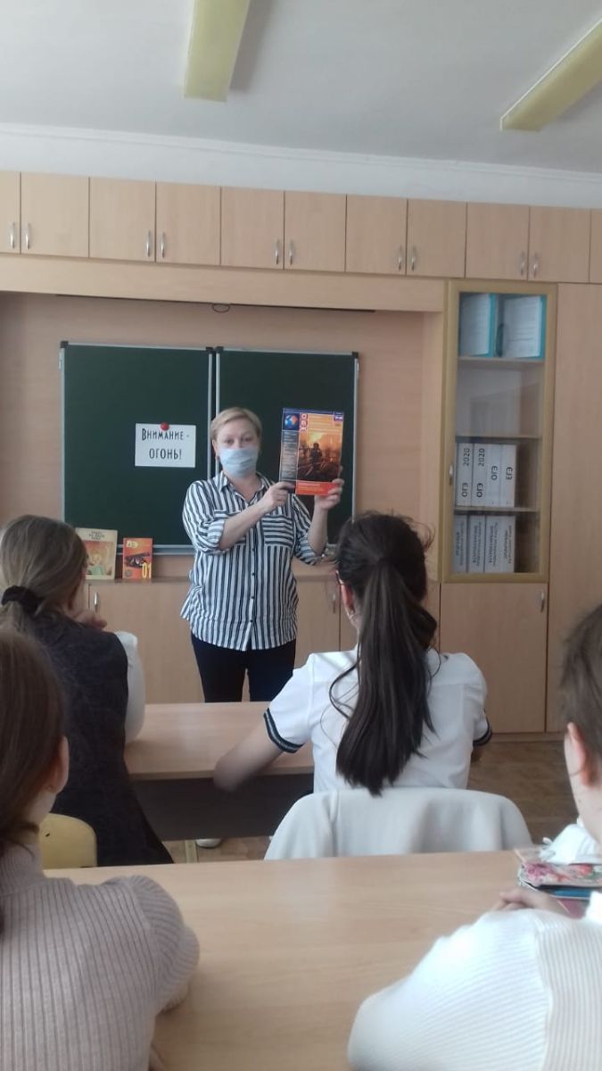 Перед детьми в классе стоит библиотекраь и показывает  им книгу